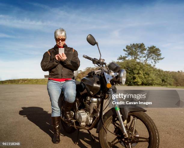 senior woman using smart phone while standing by motorcycle on road - old motorcycles bildbanksfoton och bilder