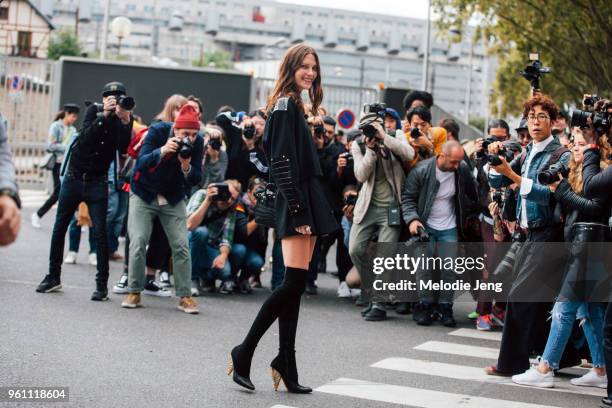 Top model Cat McNeil is surrounded by photographers and wears an all black outfit including a military-style sweater, short skirt, and knee high...