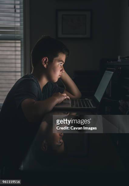 side view of serious boy using laptop computer in darkroom - dark room foto e immagini stock