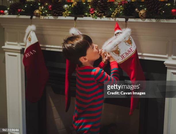 side view of curious boy looking at toy in sock hanging by fireplace during christmas - stockings stockfoto's en -beelden