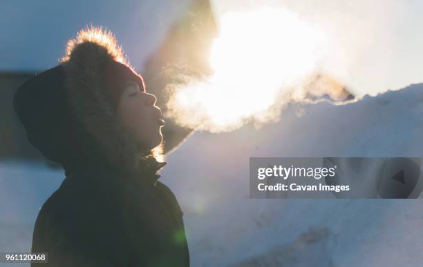 side view of boy wearing fur coat while exhaling breath vapor during winter - zichtbare adem stockfoto's en -beelden