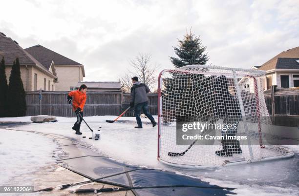 father with sons playing ice hockey at yard against sky - outdoor ice hockey stock pictures, royalty-free photos & images