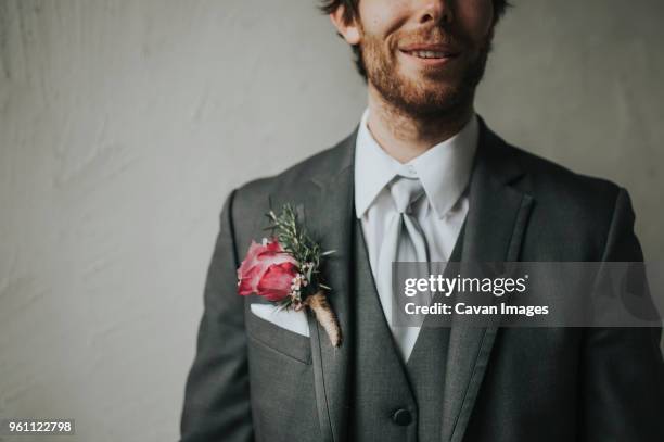 midsection of man wearing suit with boutonniere while standing against wall - ojal arreglo floral fotografías e imágenes de stock