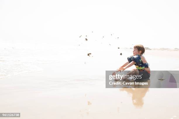 side view of boy playing with sand at beach against sky during sunny day - outer banks stockfoto's en -beelden