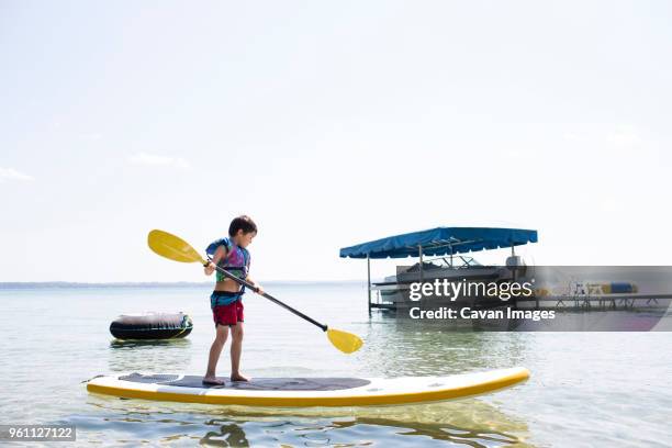 boy paddleboarding on sea against sky - life jacket isolated stock pictures, royalty-free photos & images