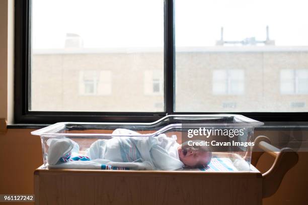 baby boy yawning while sleeping in crib by window at hospital - lettino ospedale foto e immagini stock