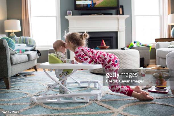side view of sister kissing brother standing in baby walker at home - baby walker stock pictures, royalty-free photos & images