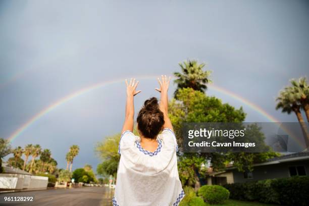 rear view of woman gesturing towards rainbow during rainy season - nur erwachsene stock-fotos und bilder