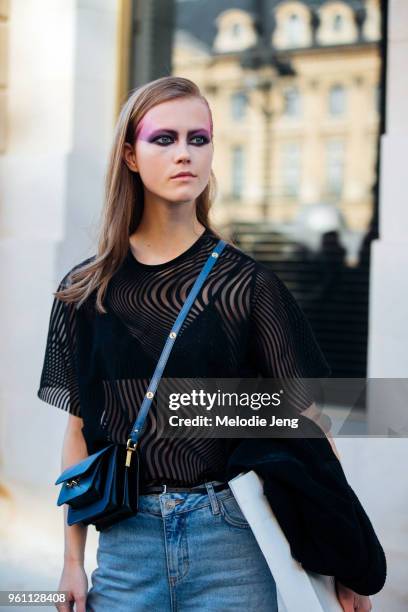 Model Julie Hoomans in pink and purple eye makeup by Pat McGrath, a translucent black top, small blue cross-body purse, and blue jeans after the...