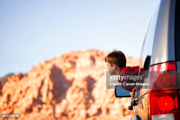 cheerful boy peeking through car window against sky - kid looking through window stock pictures, royalty-free photos & images