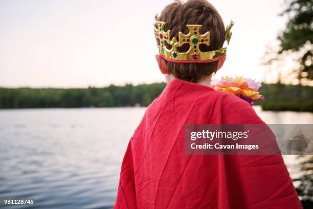 rear view of boy wearing king costume by river against clear sky - flowing cape stock-fotos und bilder