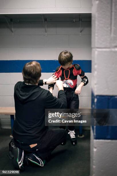 father helping son with ice hockey uniform - genderblend2015 stock pictures, royalty-free photos & images