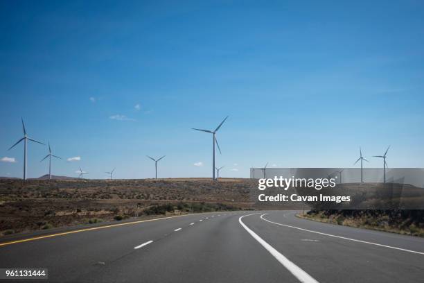 empty road and windmills against blue sky during sunny day - ellensburg stock pictures, royalty-free photos & images