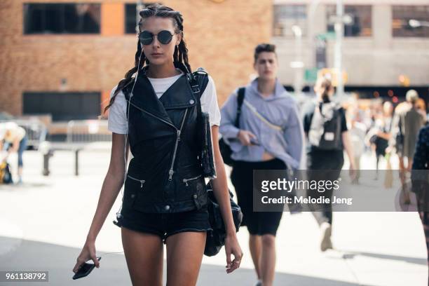Model Meaghan Waller wears circular black sunglasses, a leather vest, white tshirt, and black shorts during New York Fashion Week Spring/Summer 2018...