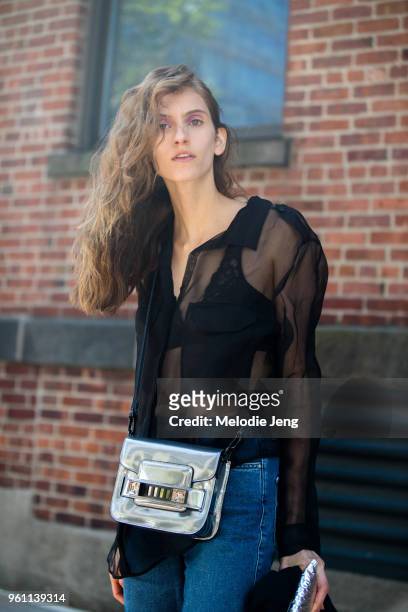Model Sarah Berger wears a black sheer top, blue jeans, and carries a silver Proenza Schouler bag during New York Fashion Week Spring/Summer 2018 on...