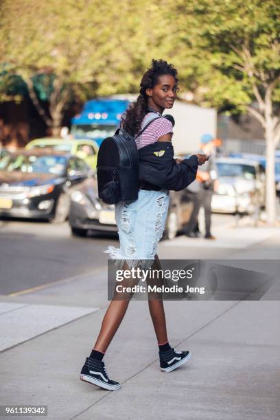 Model Tami Williams wears a black leather backpack, black Vans sneakers, a black bomber jacket off her shoulders, and denim overall shorts during New...