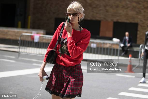 Model Veronika Vilim talks on the phone and wears thin futuristic sunglasses, a red sweatshirt, and red plaid skirt during New York Fashion Week...