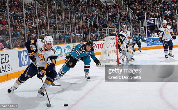 Chris Butler of the Buffalo Sabres tries to control the puck in front of netminder Ryan Miller and Craig Rivet while Joe Thornton of the San Jose...