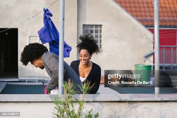 young beautiful couple hanging up laundry on rooftop terrace - afro man washing stock pictures, royalty-free photos & images