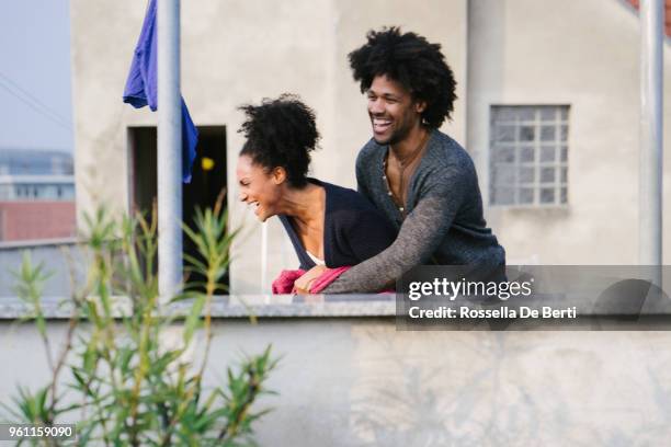 young beautiful couple hanging up laundry on rooftop terrace - afro man washing stock pictures, royalty-free photos & images