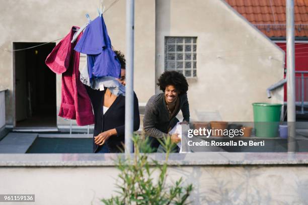 young beautiful couple hanging up laundry on rooftop terrace - afro man washing stock pictures, royalty-free photos & images