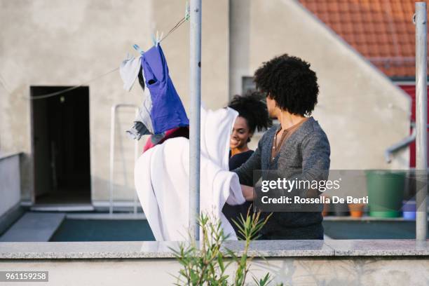 young beautiful couple hanging up laundry on rooftop terrace - afro man washing stock pictures, royalty-free photos & images