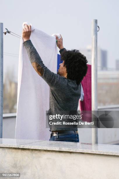young beautiful man hanging up laundry on rooftop terrace - afro man washing stock pictures, royalty-free photos & images