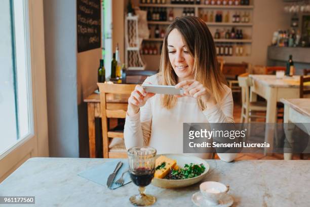 woman taking photo of vegan meal in restaurant - woman salad stockfoto's en -beelden