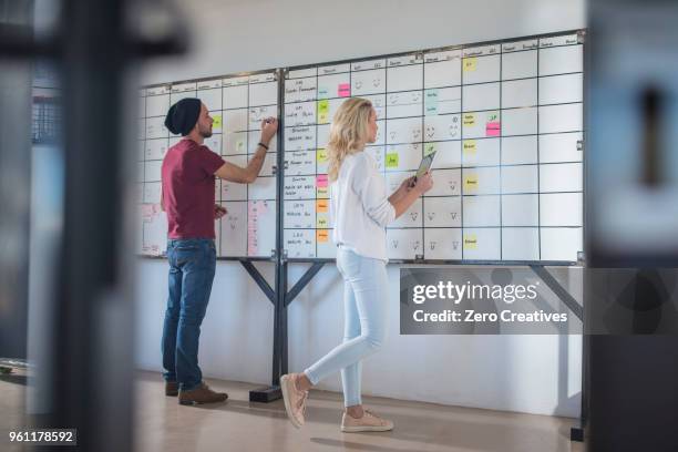 male and female colleague planning ideas on office whiteboard - topnews foto e immagini stock