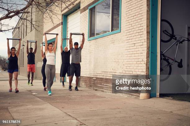 group of people with arms raised carrying weights equipment, front view - heshphoto fotografías e imágenes de stock