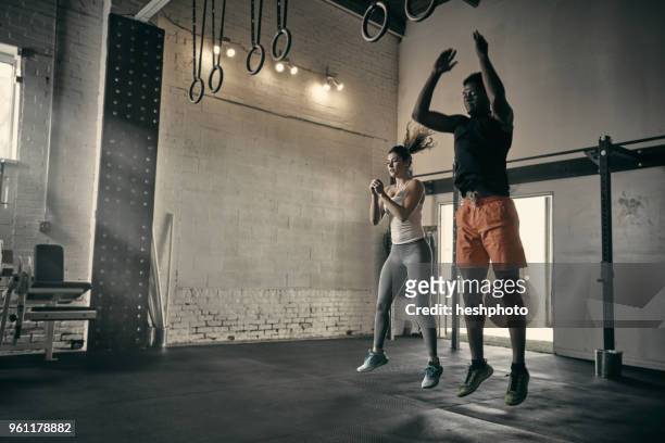 man and woman in gym jumping in mid air - heshphoto stock-fotos und bilder