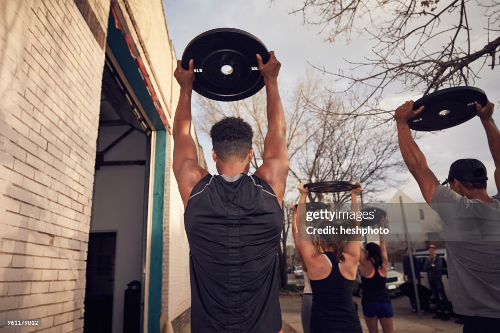 Rear view of people with arms raised carrying weights equipment