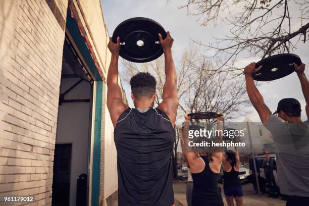 rear view of people with arms raised carrying weights equipment - heshphoto fotografías e imágenes de stock