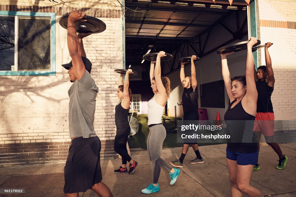 Group of people with arms raised carrying weights equipment, side view