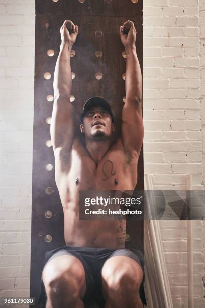 man in gym using exercise equipment, doing leg pull ups - heshphoto stock-fotos und bilder