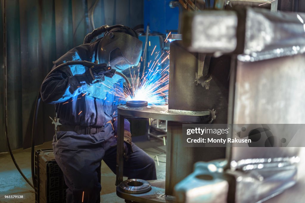 Welder welding part of digger bucket in engineering factory