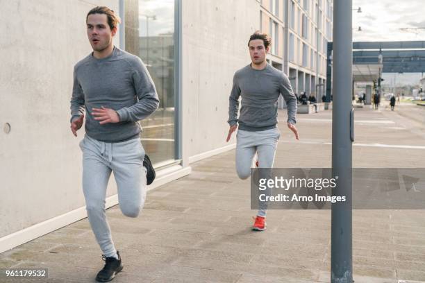 young adult male twin runners, running along city sidewalk - chándal fotografías e imágenes de stock