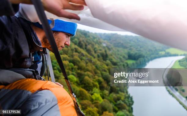young male rock climber looking out from rock face portaledge looking out at river meuse, freyr, belgium, elevated view - meuse river stockfoto's en -beelden