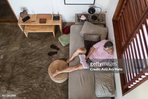 mature man on sofa reading book, overhead view - reading glasses top view stock pictures, royalty-free photos & images