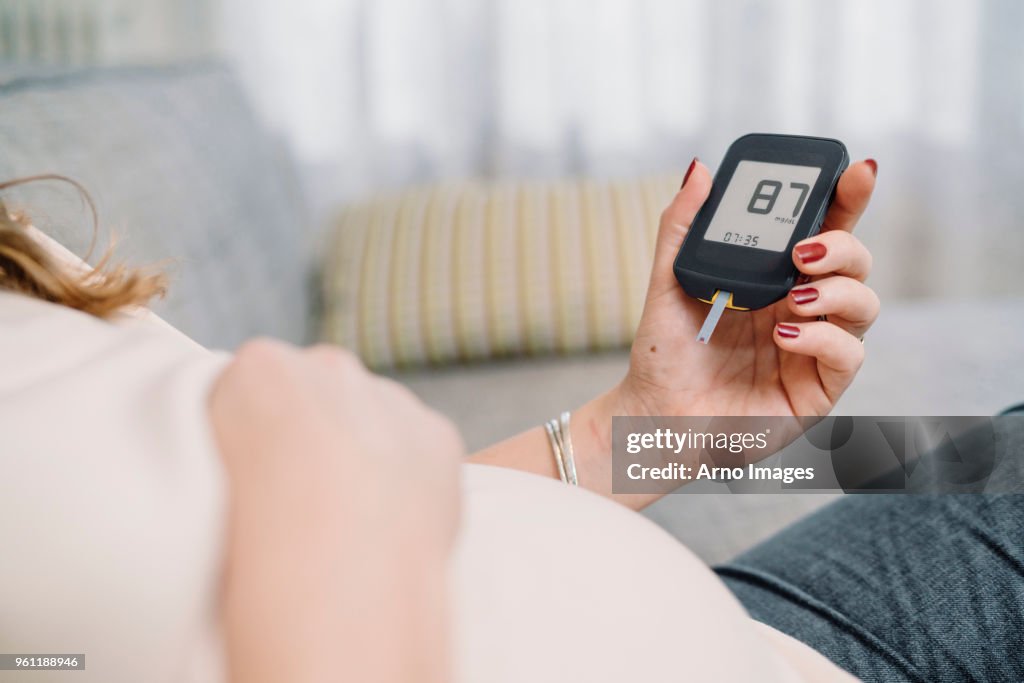 Pregnant woman on sofa looking at blood sugar test, cropped