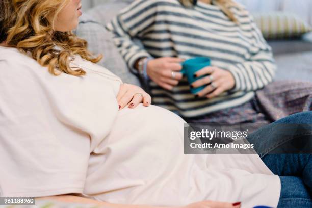 pregnant woman and friend on sofa, cropped - female friendship stock pictures, royalty-free photos & images