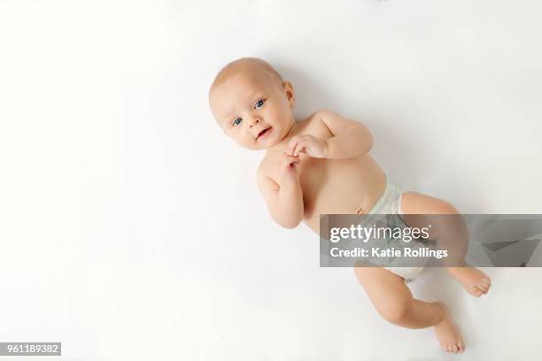 overhead view of baby boy lying on white background looking at camera - windel stock-fotos und bilder