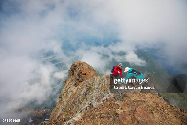 high angle view of hiker helping friend on mountain amidst clouds - doing a favor - fotografias e filmes do acervo