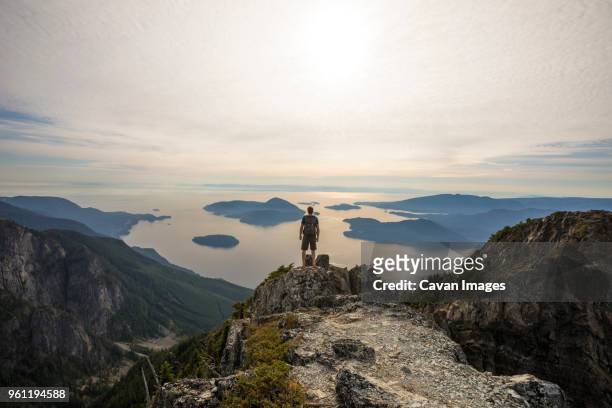 carefree hiker with backpack looking at view while standing on mountain against sky - vancouver sunset stock pictures, royalty-free photos & images