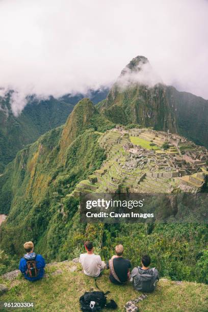 rear view of friends sitting on mountain against machu picchu - machu picchu stock-fotos und bilder