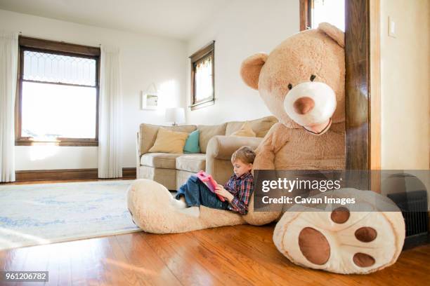 side view of boy playing game while sitting on large teddy bear at home - life of teddy stock-fotos und bilder