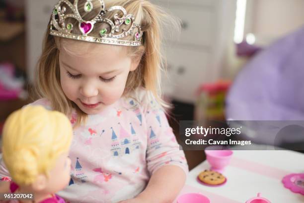 girl wearing crown while playing with doll at home - doll house stockfoto's en -beelden