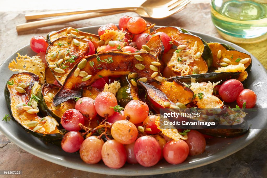 Close-up of red grapes with acorn squash in plate on table