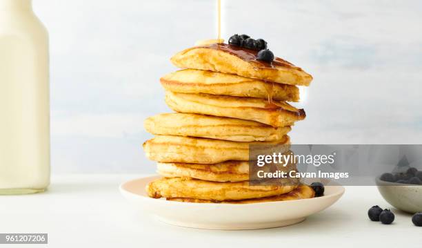 stack of pancakes with blueberries and maple syrup in plate on table - maple syrup pancakes stockfoto's en -beelden