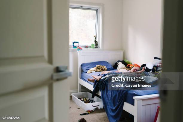 boy sleeping on bed at home seen through doorway - messy bedroom 個照片及圖片檔